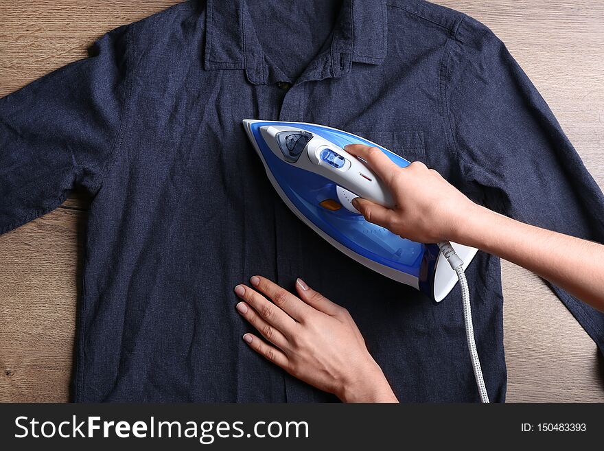 Woman ironing shirt on wooden background, top view