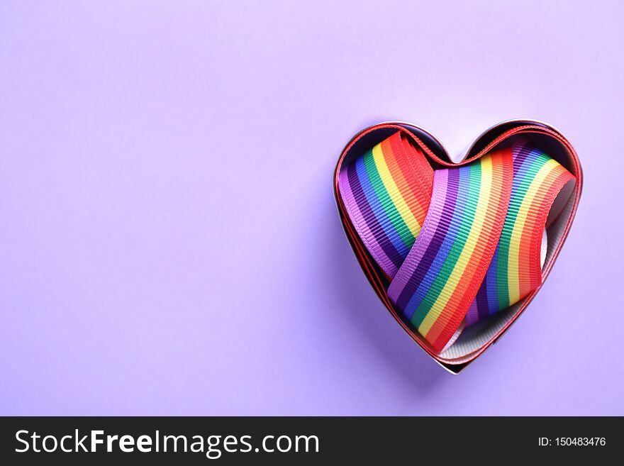 Heart shaped mold and bright rainbow ribbon on color background, top view. Symbol of gay community