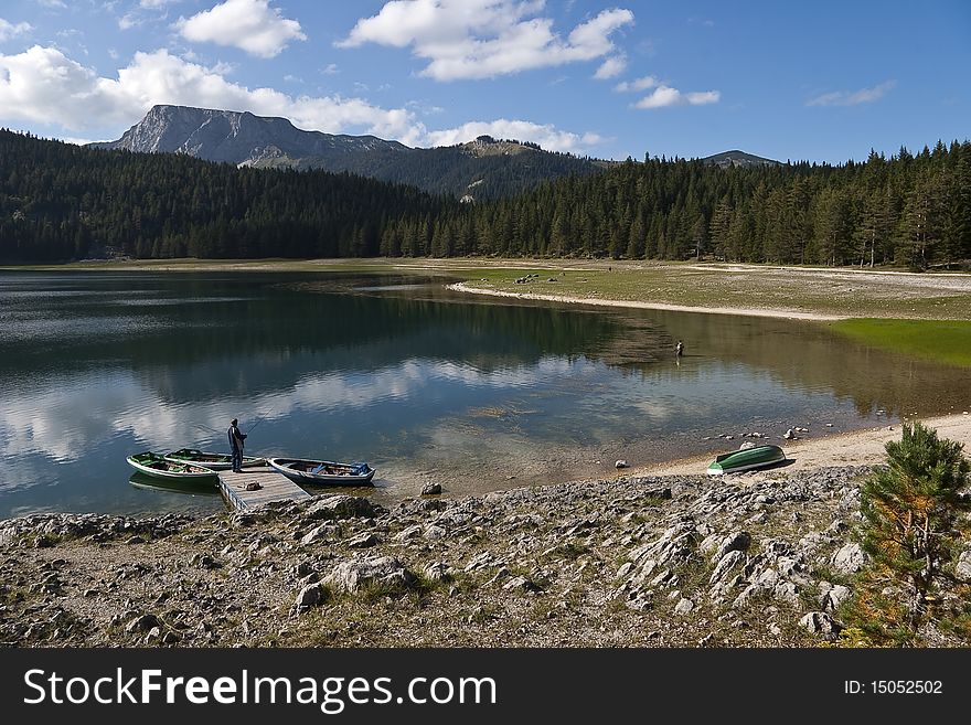 View of Black lake in Durmitor National park with stony coast, boats and fishermen, Montenegro. View of Black lake in Durmitor National park with stony coast, boats and fishermen, Montenegro
