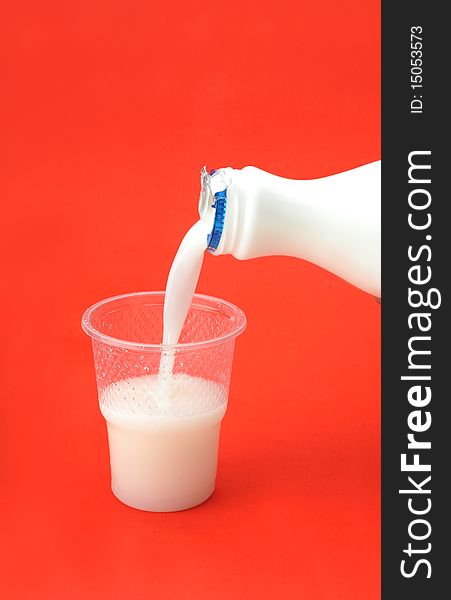 Milk inflow plastic cup over red background