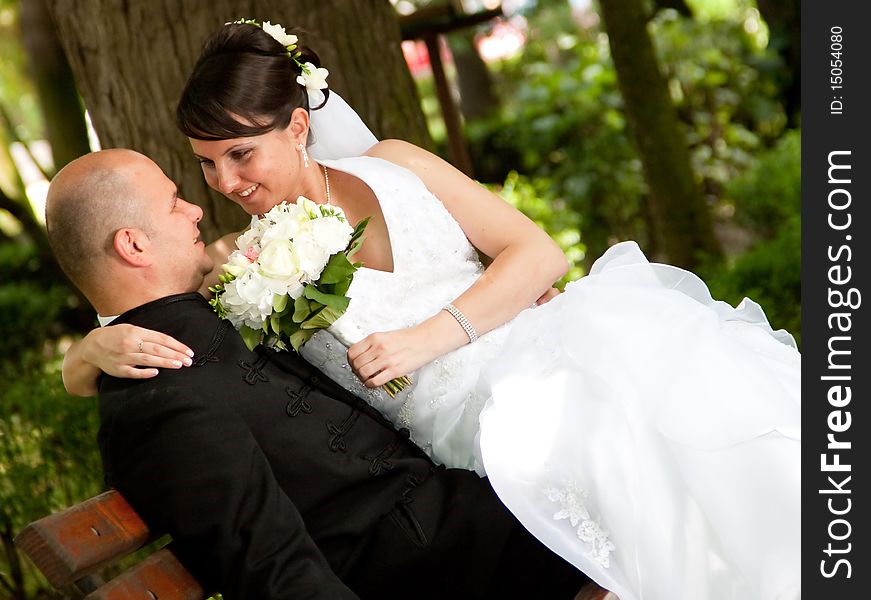 Bride and groom sitting on bench in park