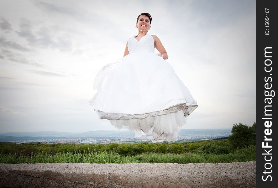 Happy bride jumping against blue sky