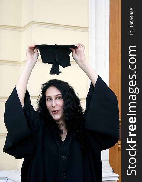 Young student in gown near the university trying on the cap. Young student in gown near the university trying on the cap