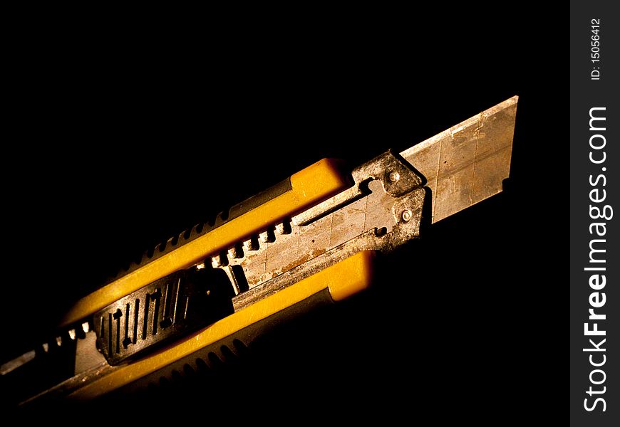 Automatic cutting tool / knife / cutter in yellow casing. Rusty blade. Black / dark background.