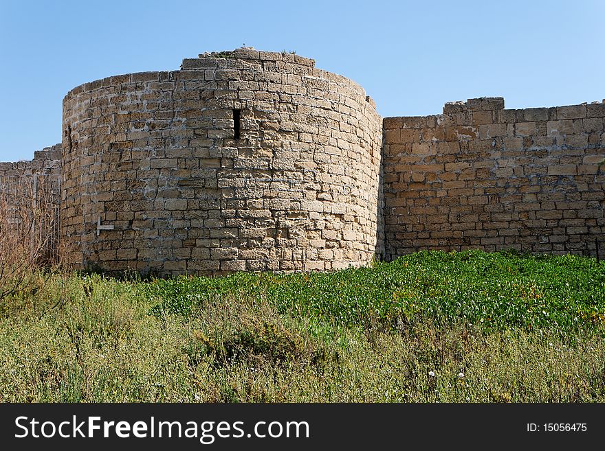 Round tower and wall of medieval castle among grass