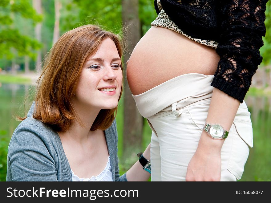 Girl listening pregnant belly. Outdoor shot