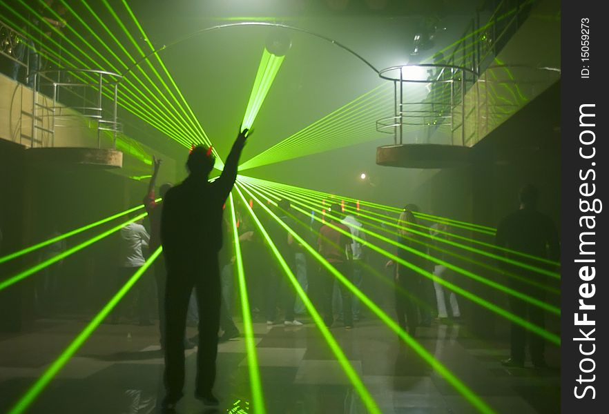 The young man in night club holds a ray of light against laser show and dancing crowd. The young man in night club holds a ray of light against laser show and dancing crowd