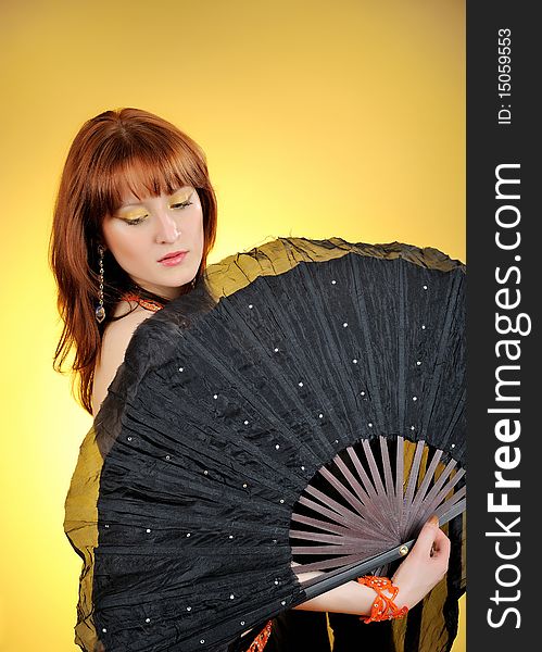 Beautiful belly dancer with big black fan. yellow background