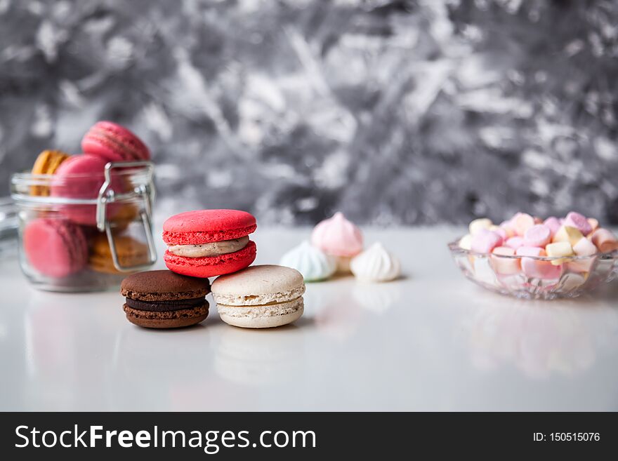 Colorful macaroons in a glass jar with marshmallows on the white table. Colorful macaroons in a glass jar with marshmallows on the white table