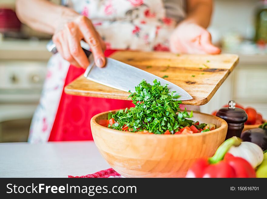 Female hand put chopped parsley in wooden bowl with salad in kitchen. Cooking vegetables