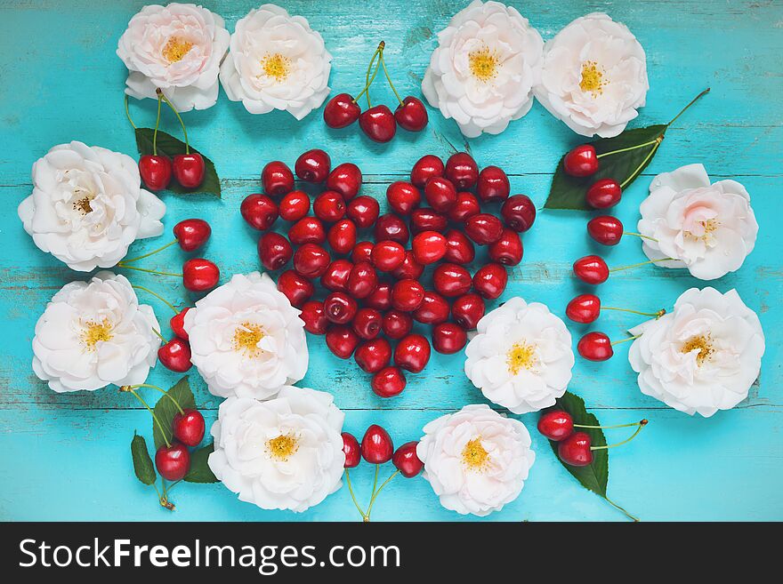 Fresh white roses with water drops, red cherry in a shape of a heart on an old painted wooden table as a bright colorful summer background for seasonal cards, posters, blogs, web design