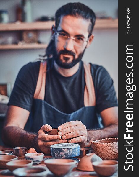 Diligent pensive man in glasses at his  pottery workshop is workig for new project.