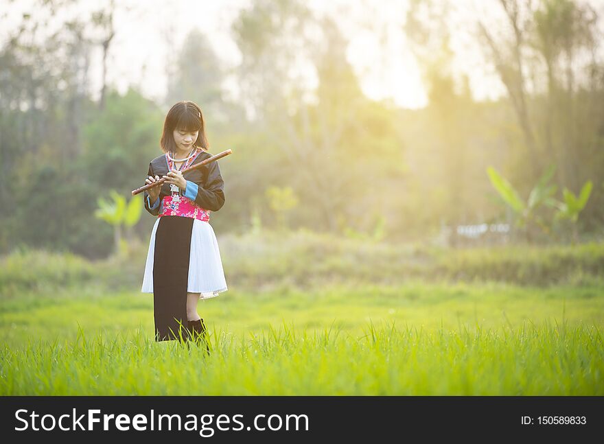 Tribe asian lady girl in custom dress hand hold flute with happy face walking in rice field in monsoon period
