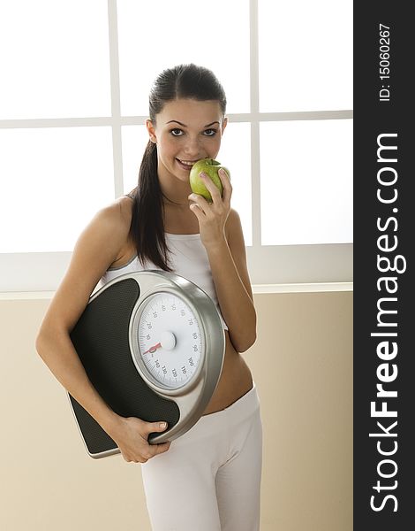 Young woman holding weight scale and eating apple