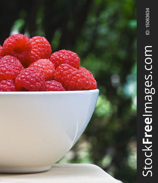 A white bowl of ripe strawberries on a cutting board on green background