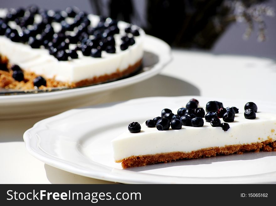 Blueberry cheesecake slice on a plate with the whole cake in the background
