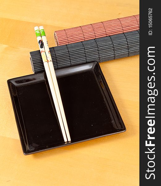 Two rolled bamboo mats with a square black plate and chopsticks. Two rolled bamboo mats with a square black plate and chopsticks