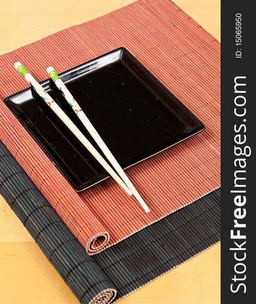 Oriental dining concept through black square plate and chopsticks on bamboo place mats. Oriental dining concept through black square plate and chopsticks on bamboo place mats