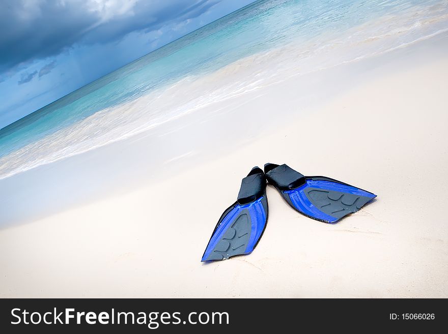 Coconut with black sunglasses and blue flippers on white sand beach in summer