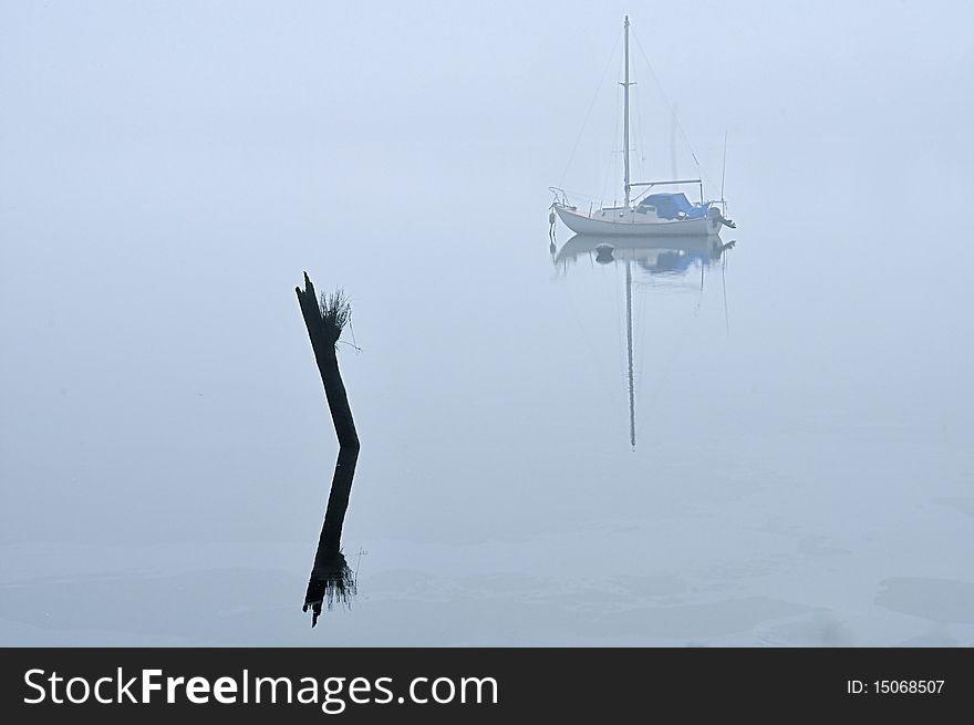 A sailboat on a foggy morning and a log sticking out of the water with reflection. A sailboat on a foggy morning and a log sticking out of the water with reflection