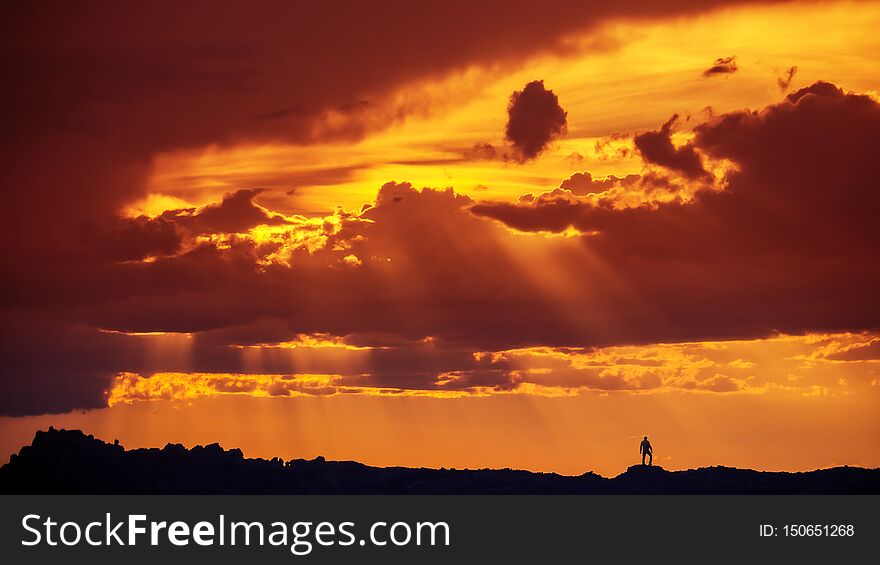 Silhouette Of Man Standing On Mountain Desert Ridge In Arches National Park Under Spectacular Sunset Clouds and Sun Rays