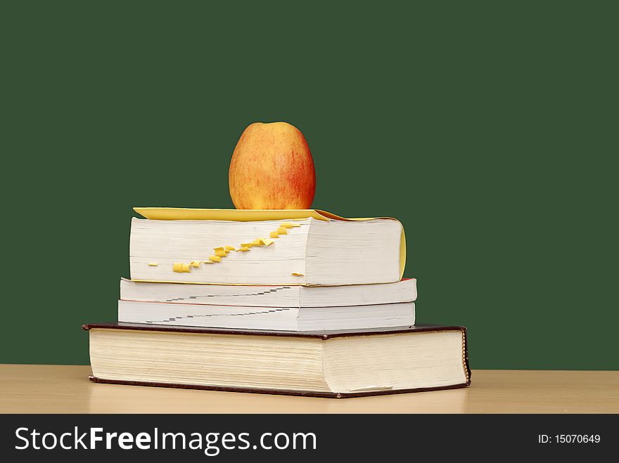 Stack of books with apple in front of green chalkboard. Stack of books with apple in front of green chalkboard