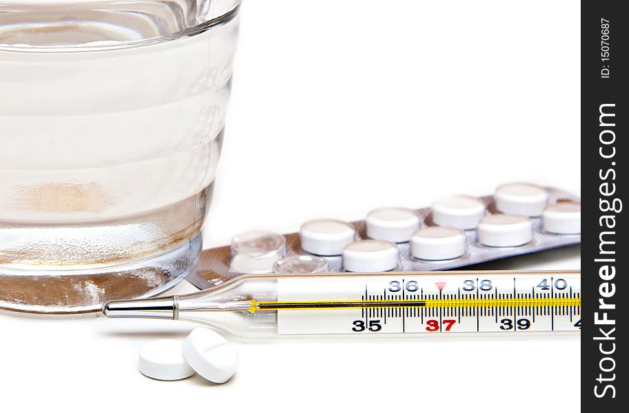 Glass with water, tablets, the medical thermometer on a white background. Glass with water, tablets, the medical thermometer on a white background