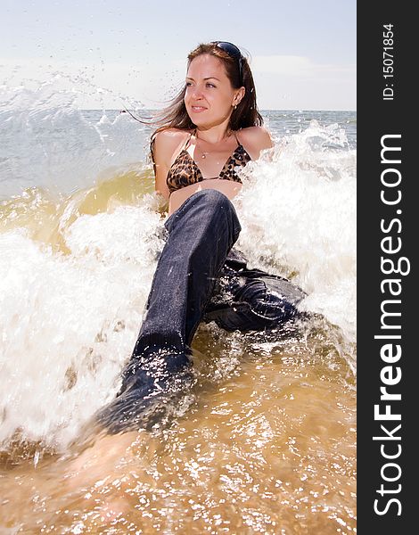 Young adult woman in jeans sits in splashes of tidal waves of a sea. Young adult woman in jeans sits in splashes of tidal waves of a sea