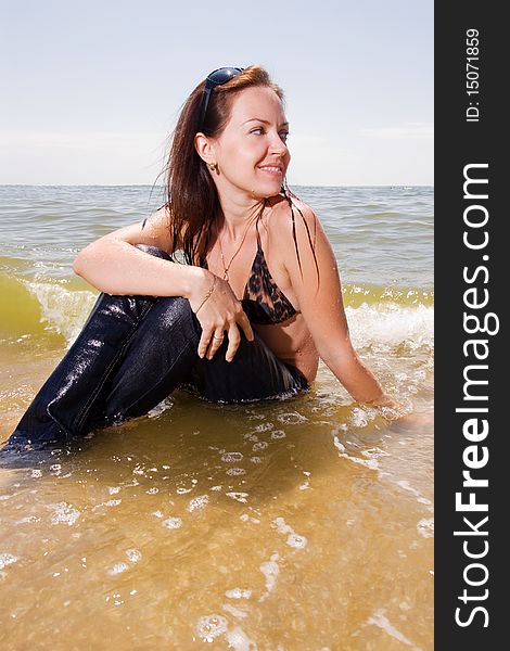 Young adult woman in wet jeans sits in splashes of tidal waves of a sea smiling. Young adult woman in wet jeans sits in splashes of tidal waves of a sea smiling