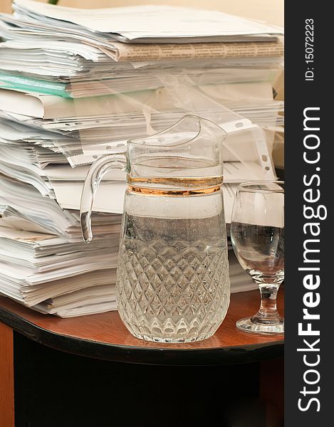 The big foot of various papers on a table at office and a decanter with potable water. The big foot of various papers on a table at office and a decanter with potable water.