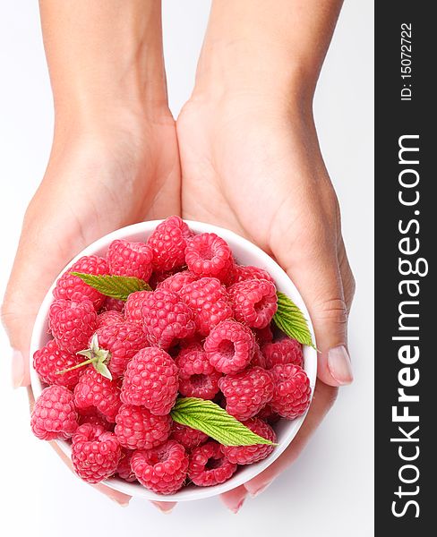 Crockery with raspberries in woman hands. Isolated on a white background.