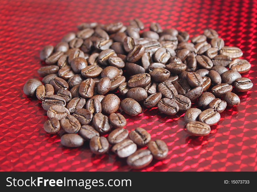 Roasted whole coffee beans scattered across a reflective red background. Roasted whole coffee beans scattered across a reflective red background