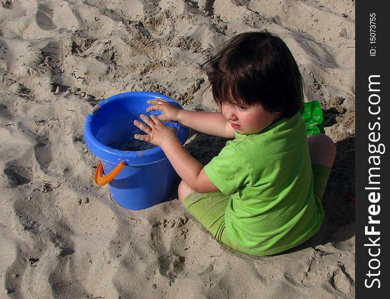 Little girl in the sandpit playing with a bucket filled with water