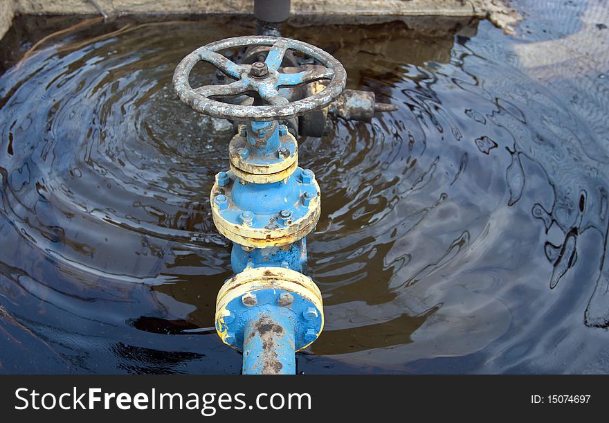 Barrel of oil over a blue tank with oil valve. Barrel of oil over a blue tank with oil valve