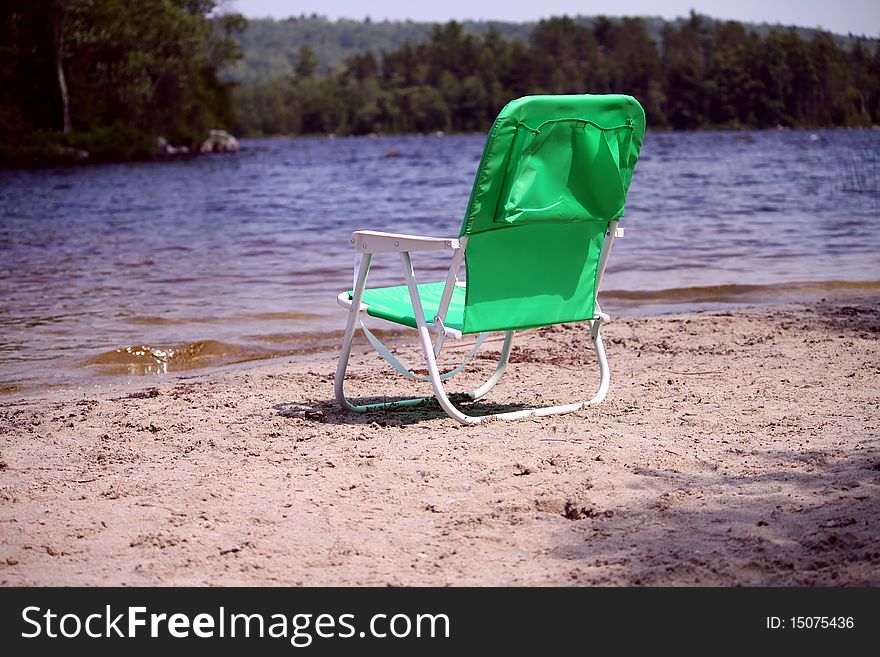 Green beach chair on sandy beach with water scenery