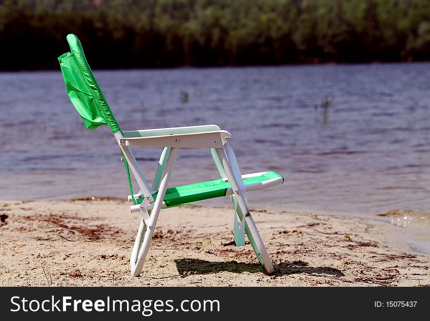 Green beach chair on sandy beach with water scenery