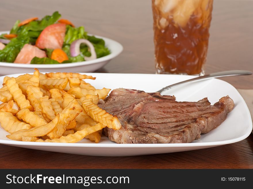 Grilled steak with french fries, a salad, and beverage. Grilled steak with french fries, a salad, and beverage