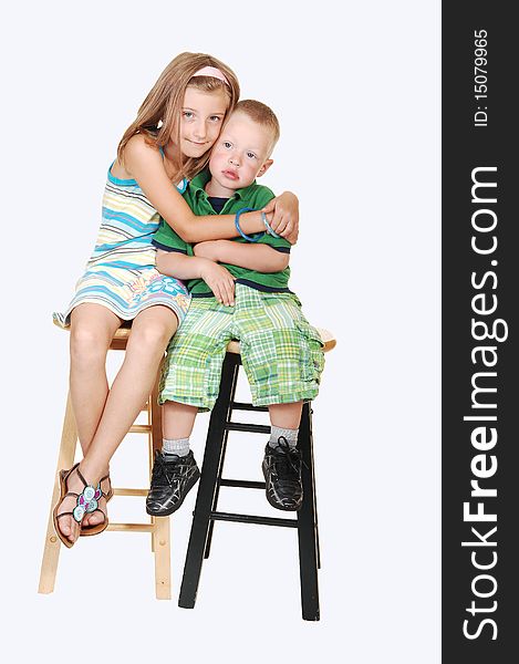 An pretty girl sitting with her brother on chairs and giving him a big hug on light blue background. An pretty girl sitting with her brother on chairs and giving him a big hug on light blue background.