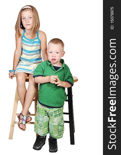 An seven year old girl sitting on a chair and her little brother standing in front of his chair in a green outfit for white background. An seven year old girl sitting on a chair and her little brother standing in front of his chair in a green outfit for white background.