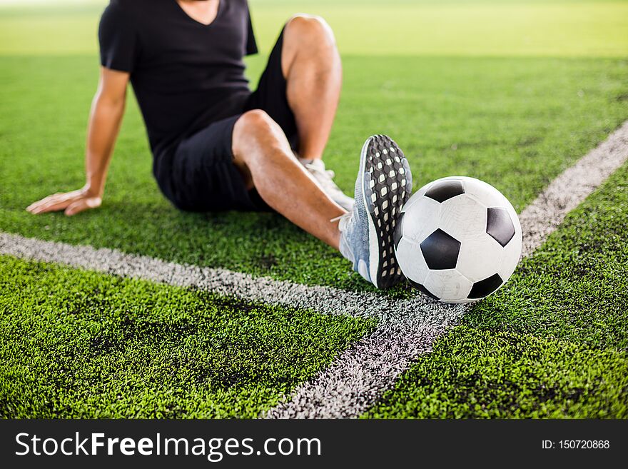 Soccer ball on green artificial turf with the player is stretch the muscles