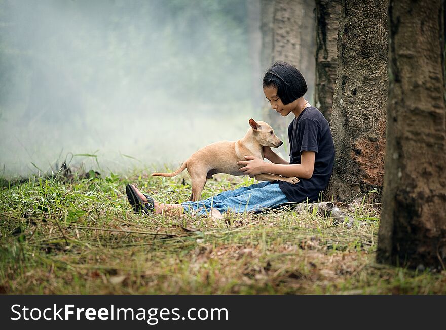 Little Asian girl sitting alone on green field under the tree with her dog, outdoor at countryside of Thailand