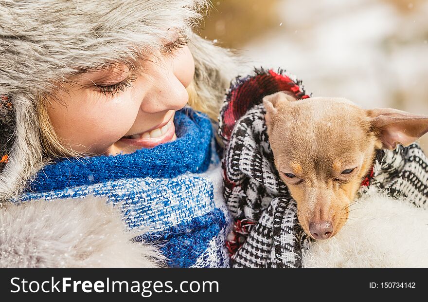 Young woman wrapped her best friend little dog in warm blanket scarf to warm him in cold snowy winter day. Animal protection save. Adoption concept. Young woman wrapped her best friend little dog in warm blanket scarf to warm him in cold snowy winter day. Animal protection save. Adoption concept
