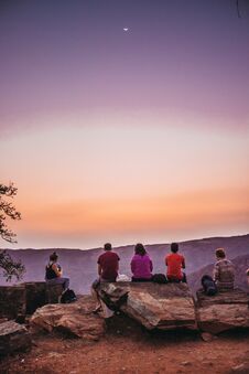 A Group Of Young Travelers Sitting On Top Of A Mountain And Watching A Beautiful View Of The Canyon Stock Image