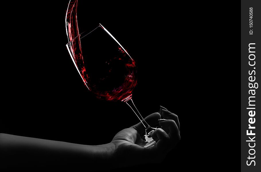 A glass of wine in hand, red wine pours into a glass, an over black background. A glass of wine in hand, red wine pours into a glass, an over black background
