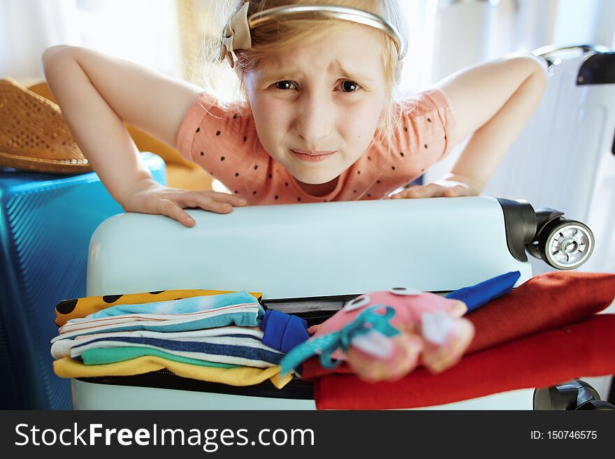 Stressed traveller girl trying to close over packed suitcase