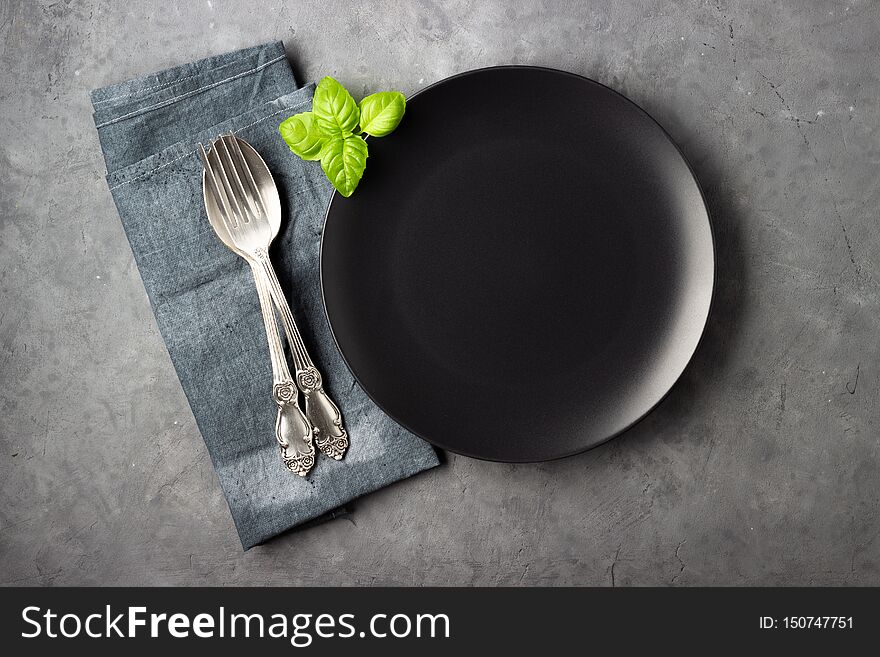 Table Setting. Black Plate, Cutlery And Napkin Over Gray Concrete Background