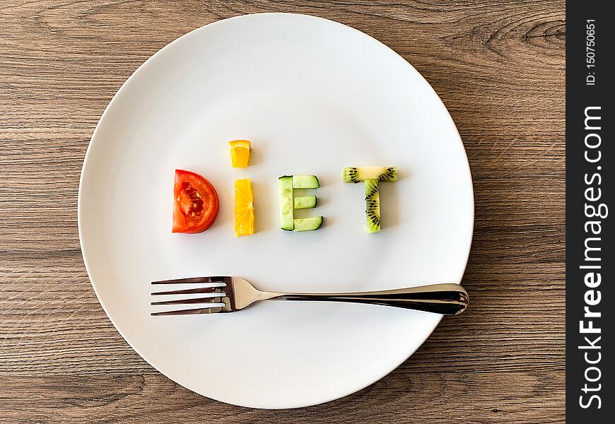 Word DIET made of sliced vegetables in plate with measuring on wood background