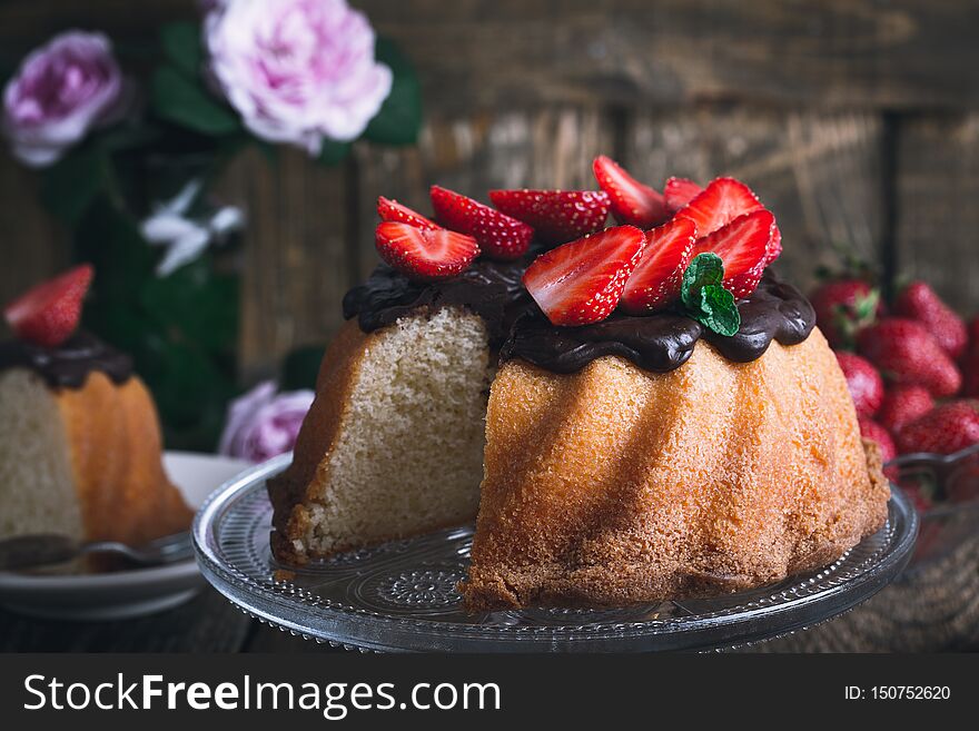 Summer cake with chocolate glaze and fresh strawberries on top on rustic wooden table, close up, selective focus