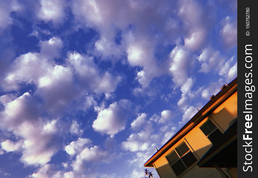 Puffy white clouds scudding across a blue sky on a sunny summer day in suburbia. A house from the suburbs. Puffy white clouds scudding across a blue sky on a sunny summer day in suburbia. A house from the suburbs.