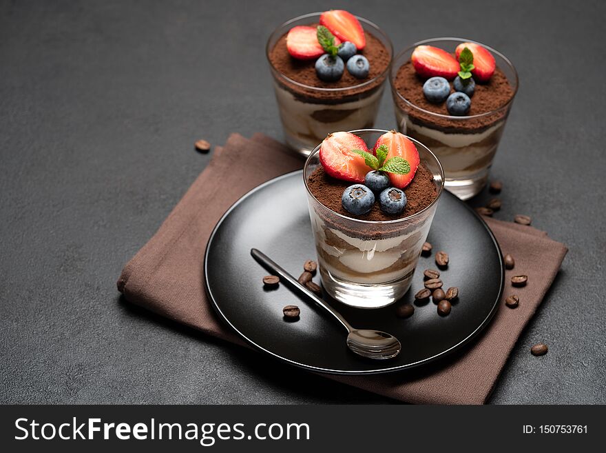 Classic tiramisu dessert with blueberries and strawberries in a glass on stone serving board on dark concrete background or table